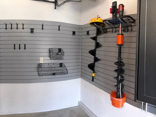 Gray slatwall holding fishing augers, hooks and baskets beside dark garage cabinets — Davenport, Iowa.
